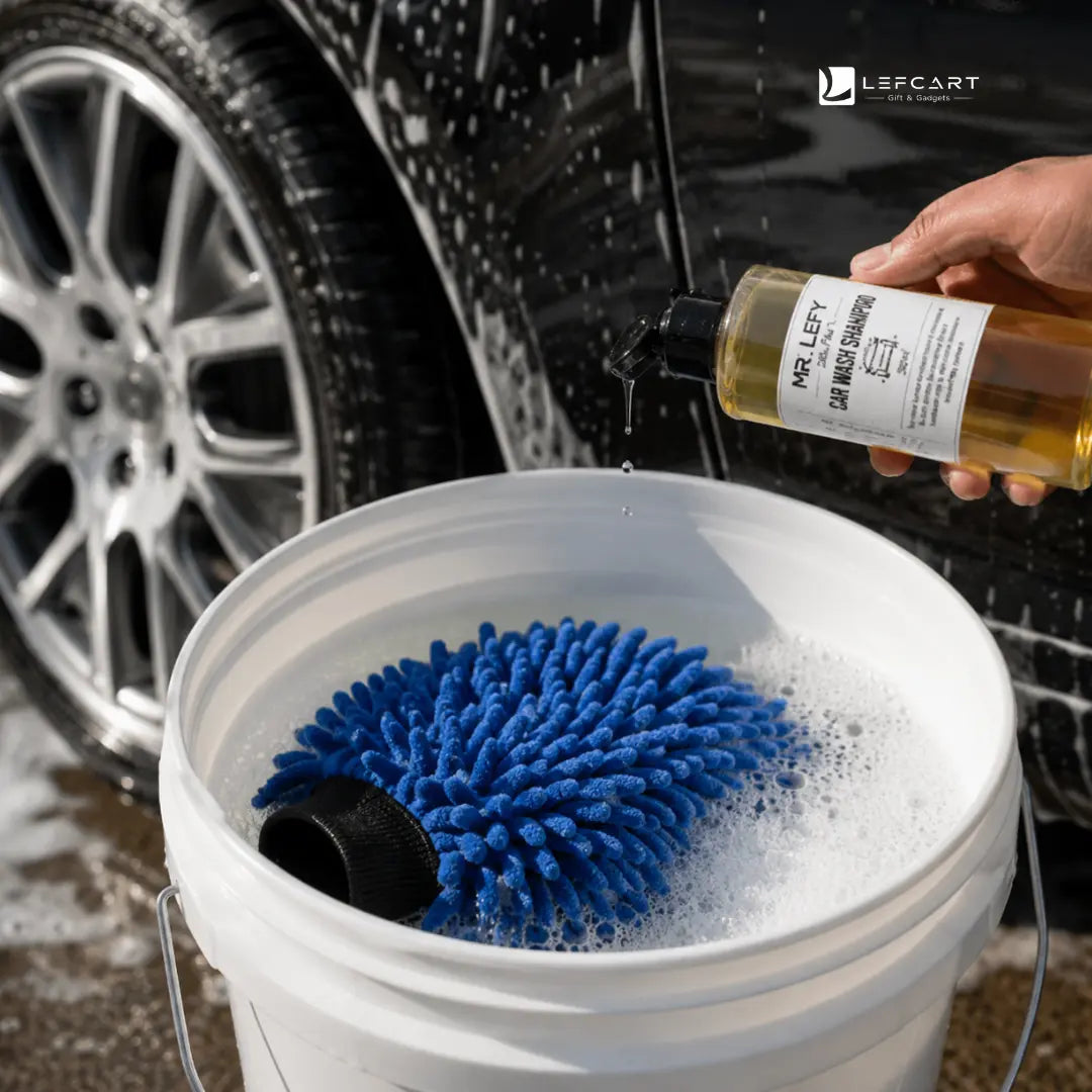 A hand holds a bottle of Lefscart Car Wash Shampoo over a white bucket containing a blue microfiber cleaning pad and soapy water, with a car wheel and body in the background.