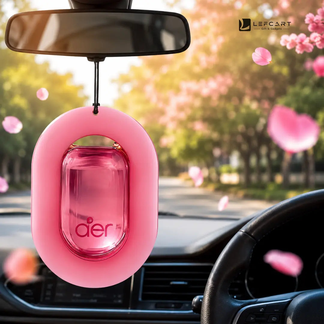 A pink car air freshener with a transparent pink center and the brand name 'dier' printed on it, hanging from a rearview mirror inside a car with blurred pink blossoms in the background.